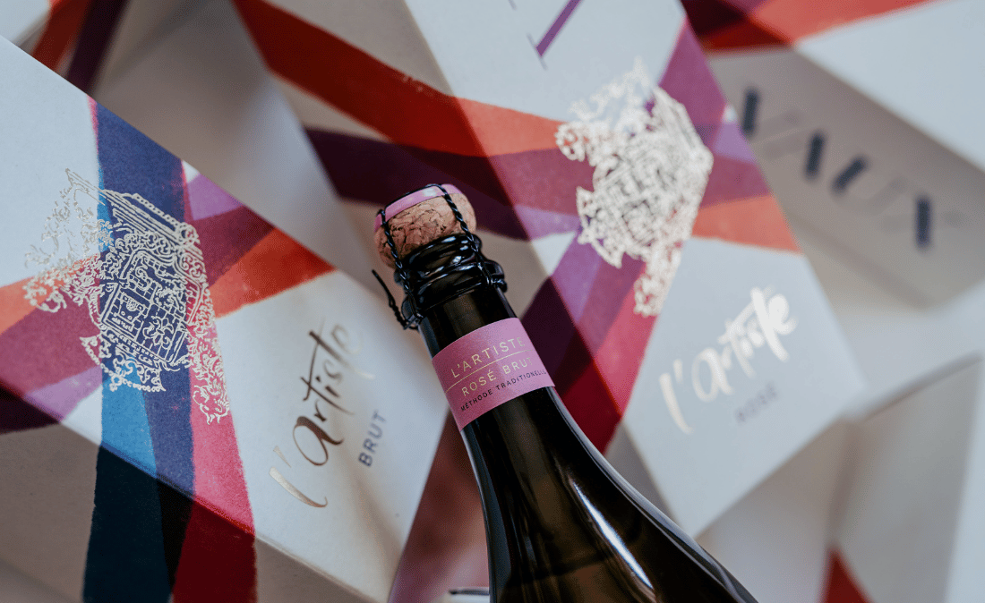 Eine Flasche l´Artiste Rosé mit Geschenkkartons im Hintergrund