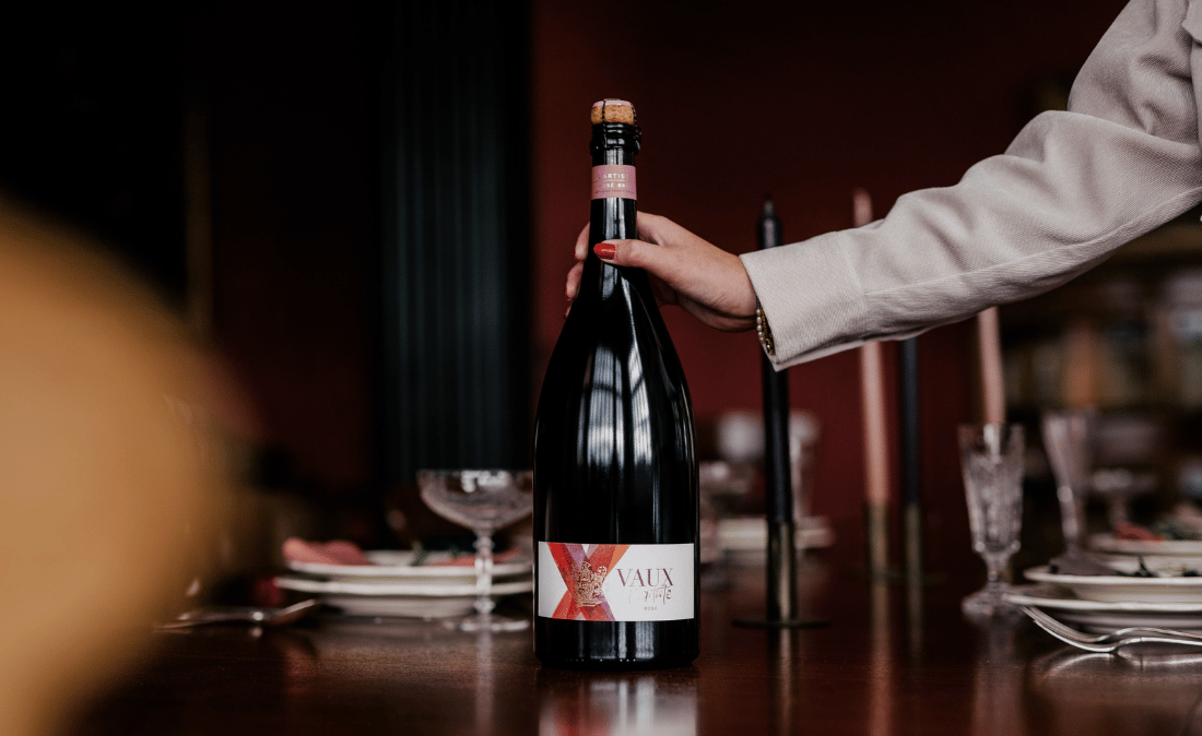 Eine Person stellt eine Magnum l´Artiste Rosé auf einen Holztisch