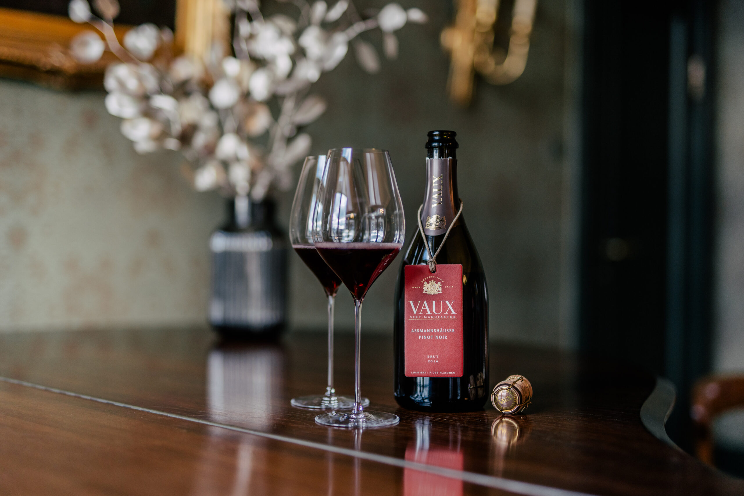 Auf einem Holztisch steht eine geöffnete Flasche Assmanshäuser Pinot Noir mit zwei gefüllten Sektgläsern