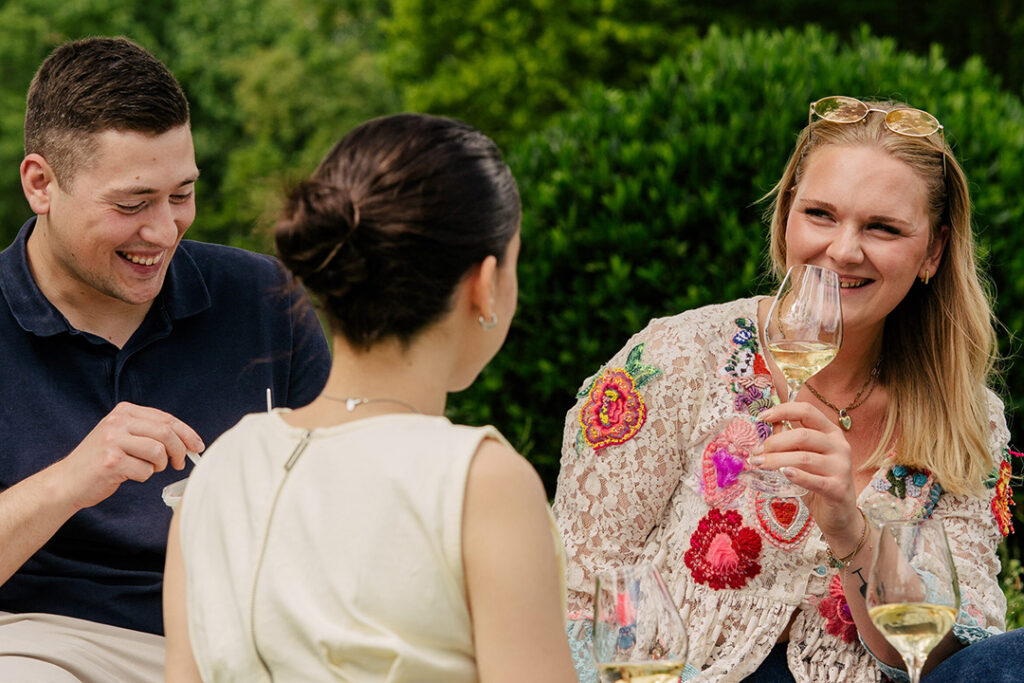 3 Personen unterhalten sich und trinken Sekt. Der Mann isst etwas.