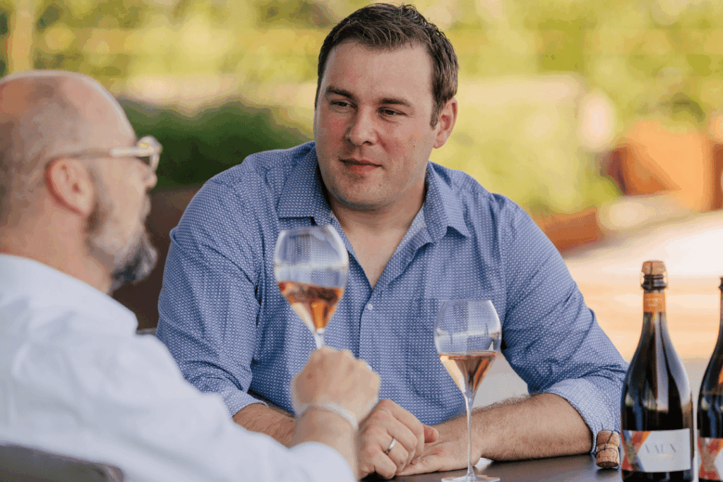 Zwei Männer die an einem Tisch sitzen und jeweils ein Glas VAUX 